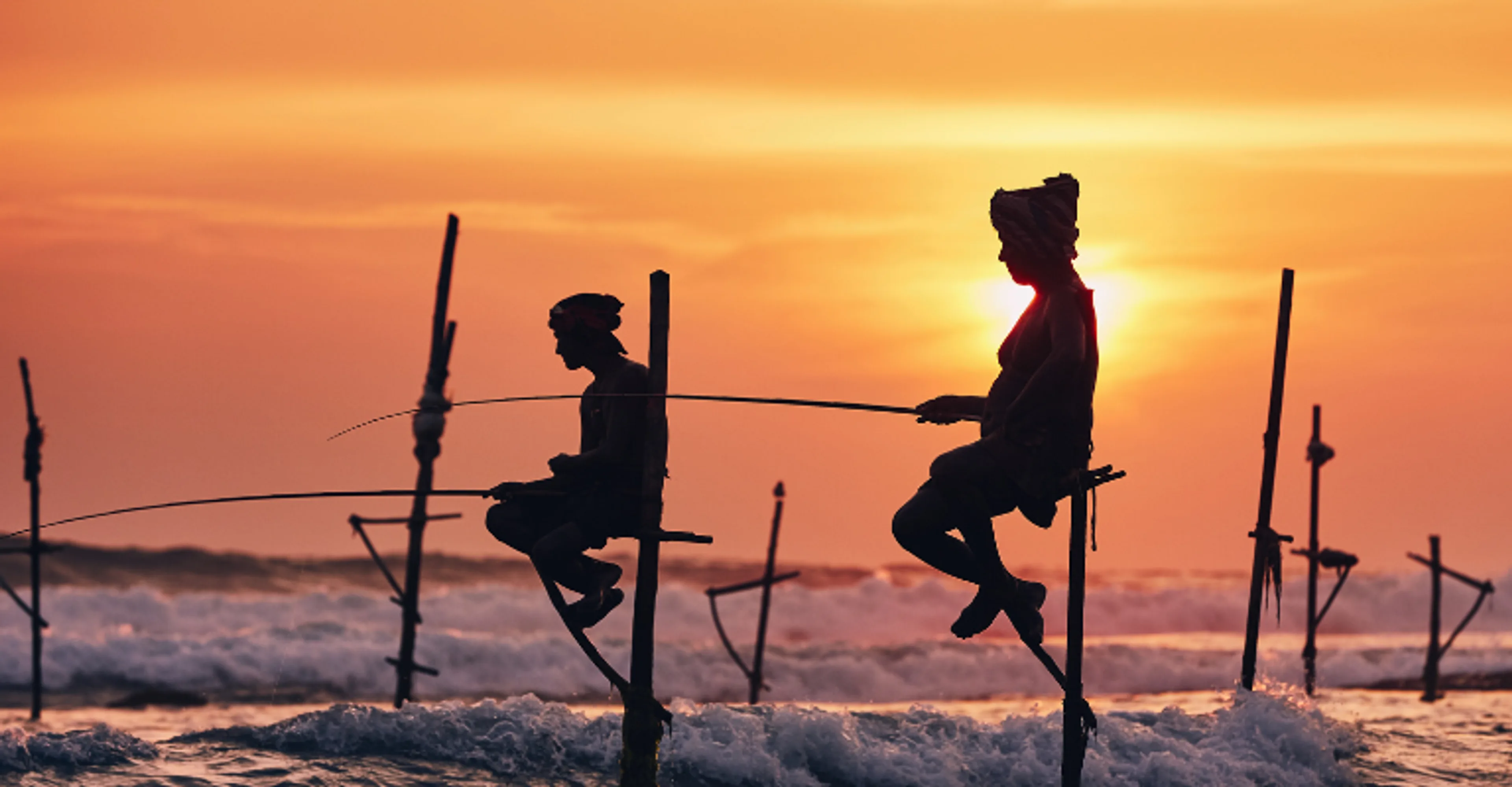 Traditional stilt fishermen silhouetted against a sunset off Sri Lanka's south coast