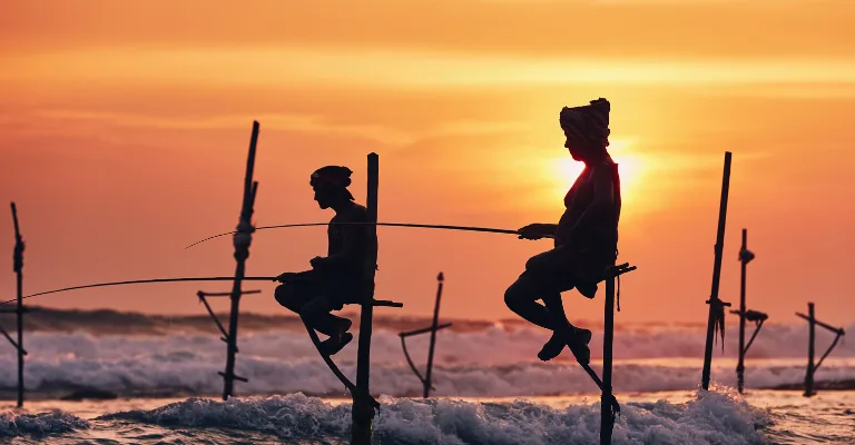Traditional stilt fishermen silhouetted against a sunset off Sri Lanka's south coast