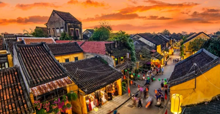 Aerial view over Hanoi's old quarter rooftops and a lantern-strung street at sunset