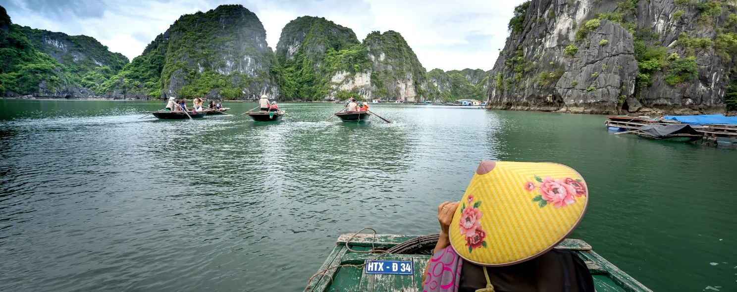 Rowboats crossing Halong Bay past limestone karsts
