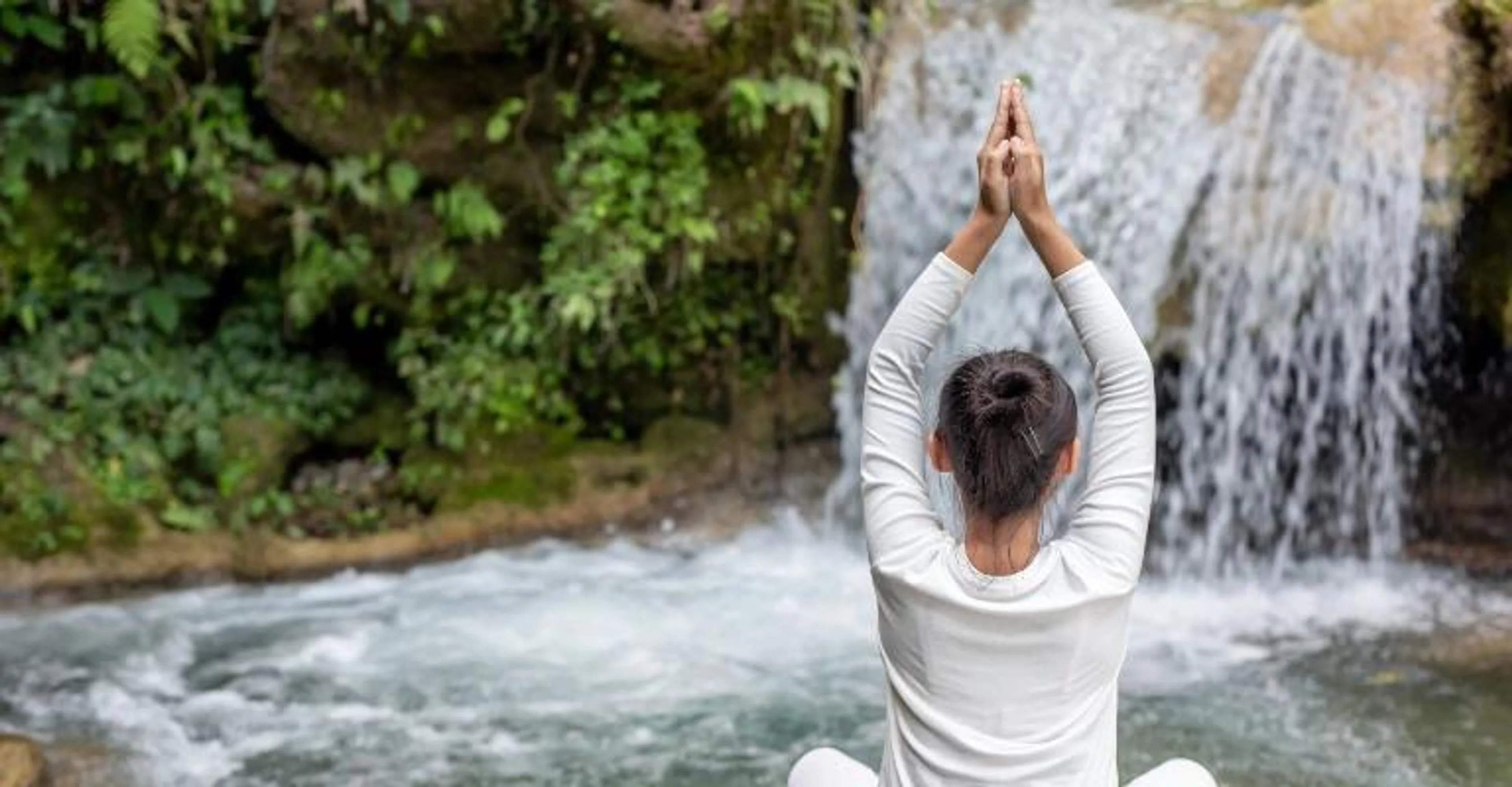 A woman practicing yoga by a waterfall.