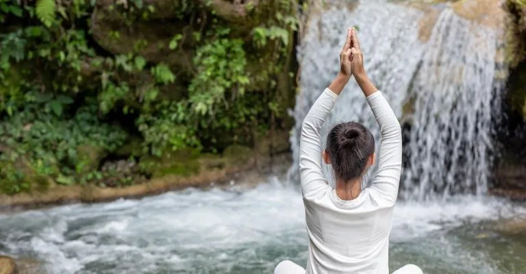 A woman practicing yoga by a waterfall.
