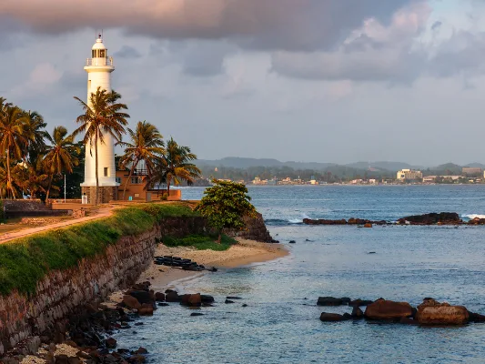 Galle Lighthouse on Sri Lanka’s coast with palm trees, ocean views, and a rocky shoreline