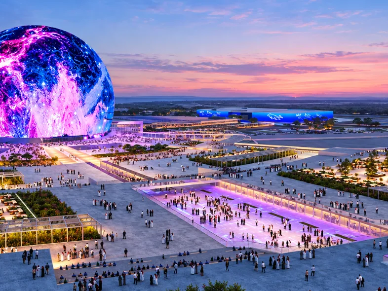 Illuminated sphere entertainment venue surrounded by crowds and plazas at dusk