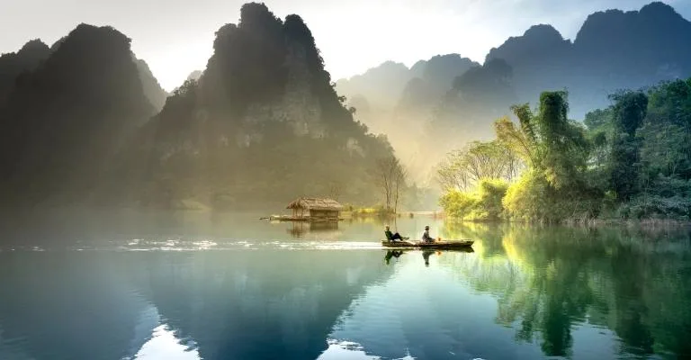 Misty limestone karsts and a stilt hut reflected on a calm river