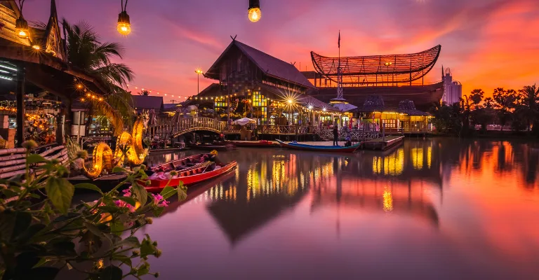 Floating market lit up at sunset with longtail boats reflected in the water, Thailand