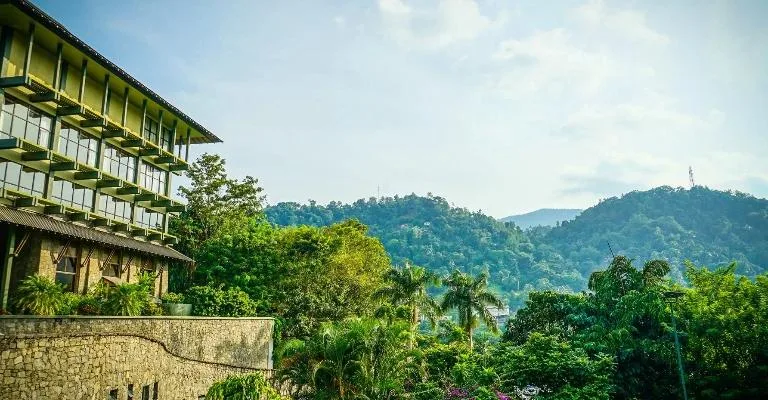 A hillside building overlooking a green valley and mountains.