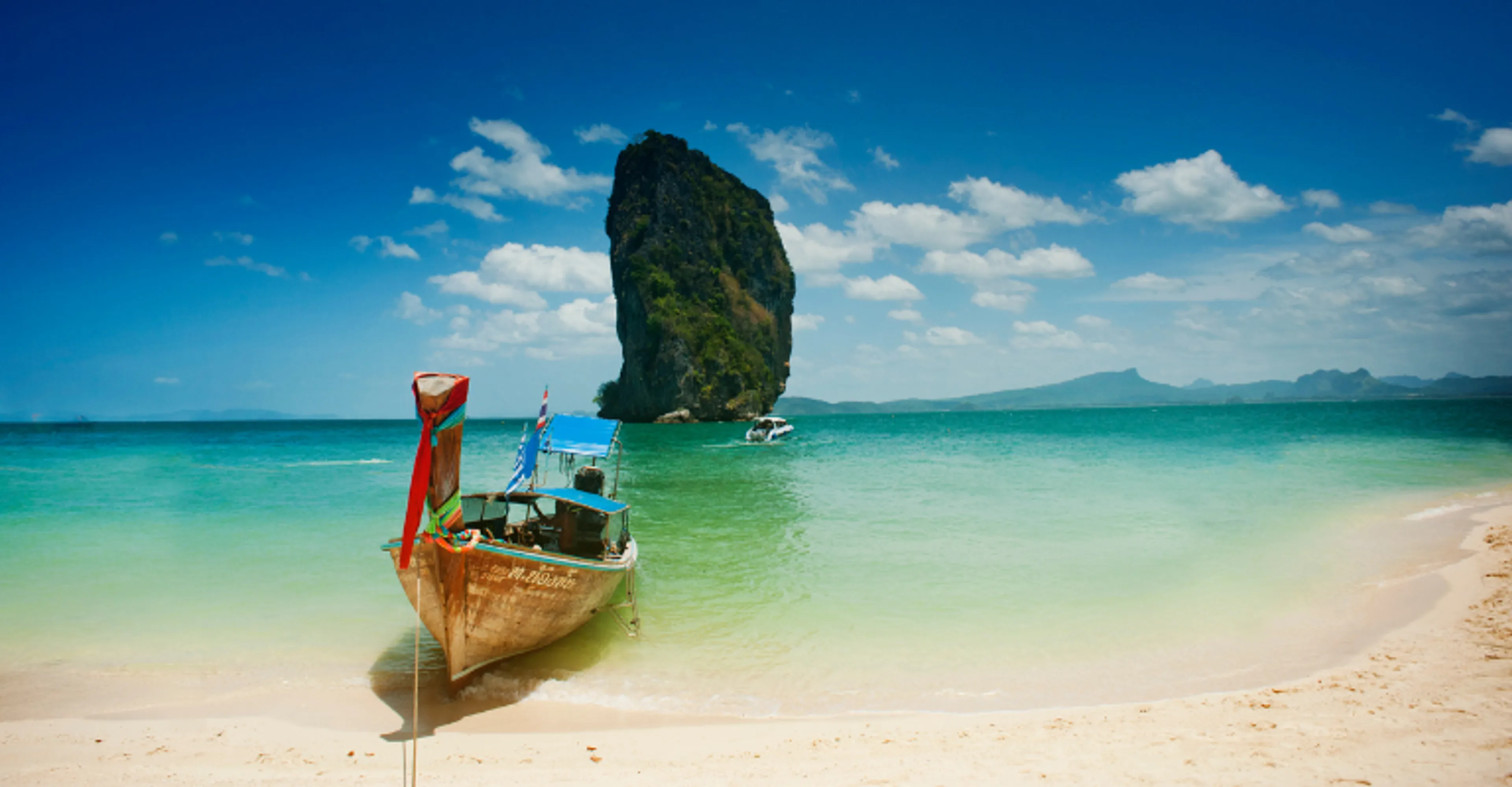 Longtail boat on a white sand beach near a limestone rock in Krabi, Thailand