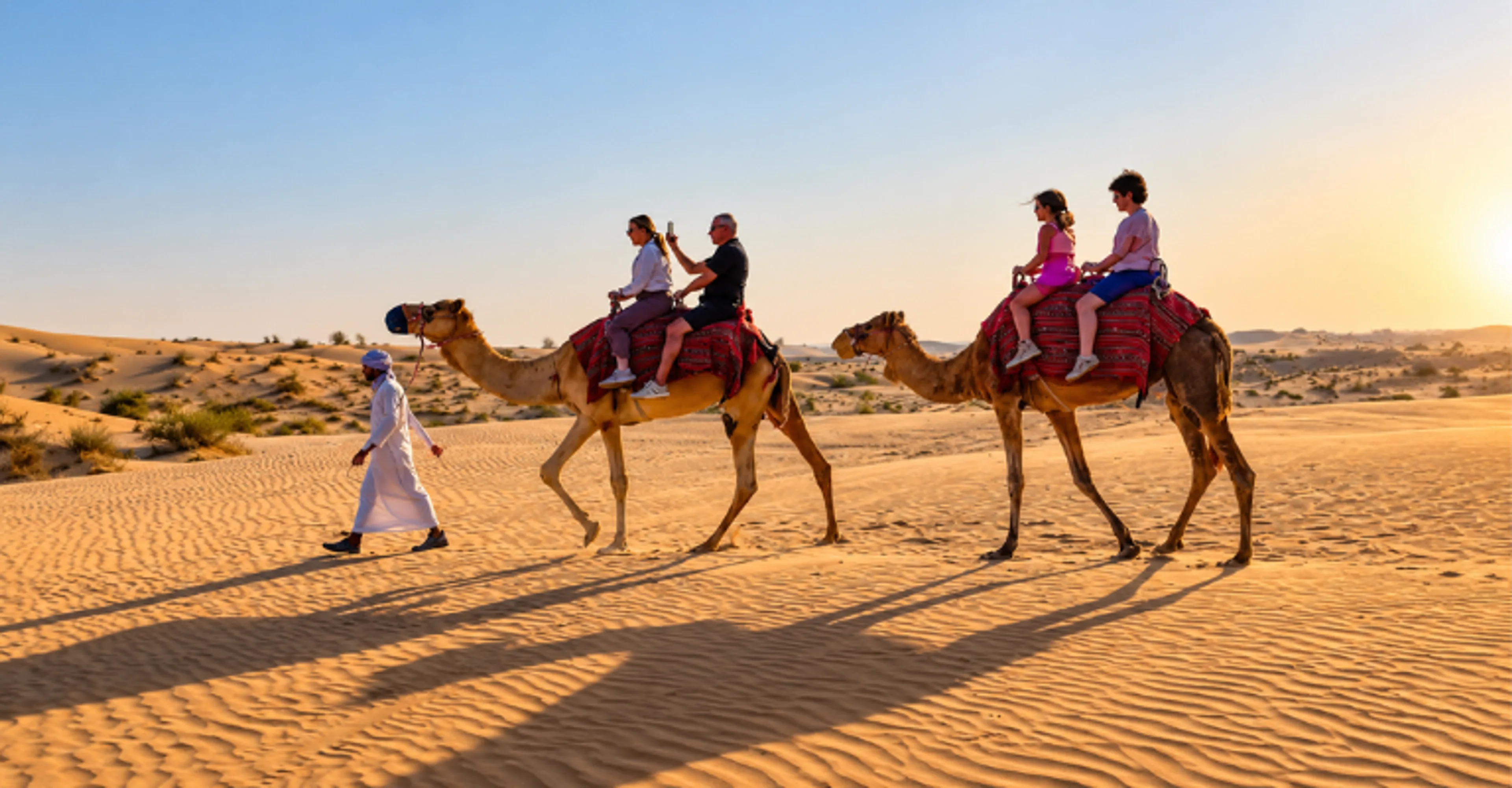Family on a camel ride in the Abu Dhabi desert at sunset