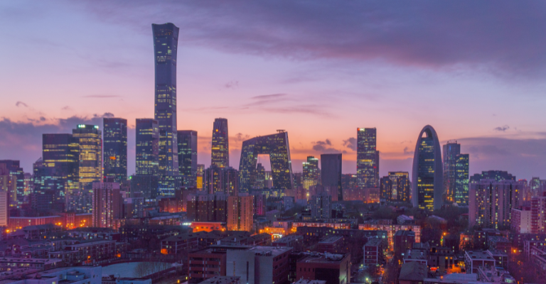 The Beijing skyline at dusk, featuring the twisted China Zun skyscraper and the distinctive loop-shaped CCTV Headquarters building, illuminated against a pink and purple sunset sky
