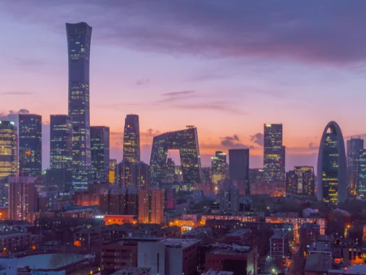 The Beijing skyline at dusk, featuring the twisted China Zun skyscraper and the distinctive loop-shaped CCTV Headquarters building, illuminated against a pink and purple sunset sky