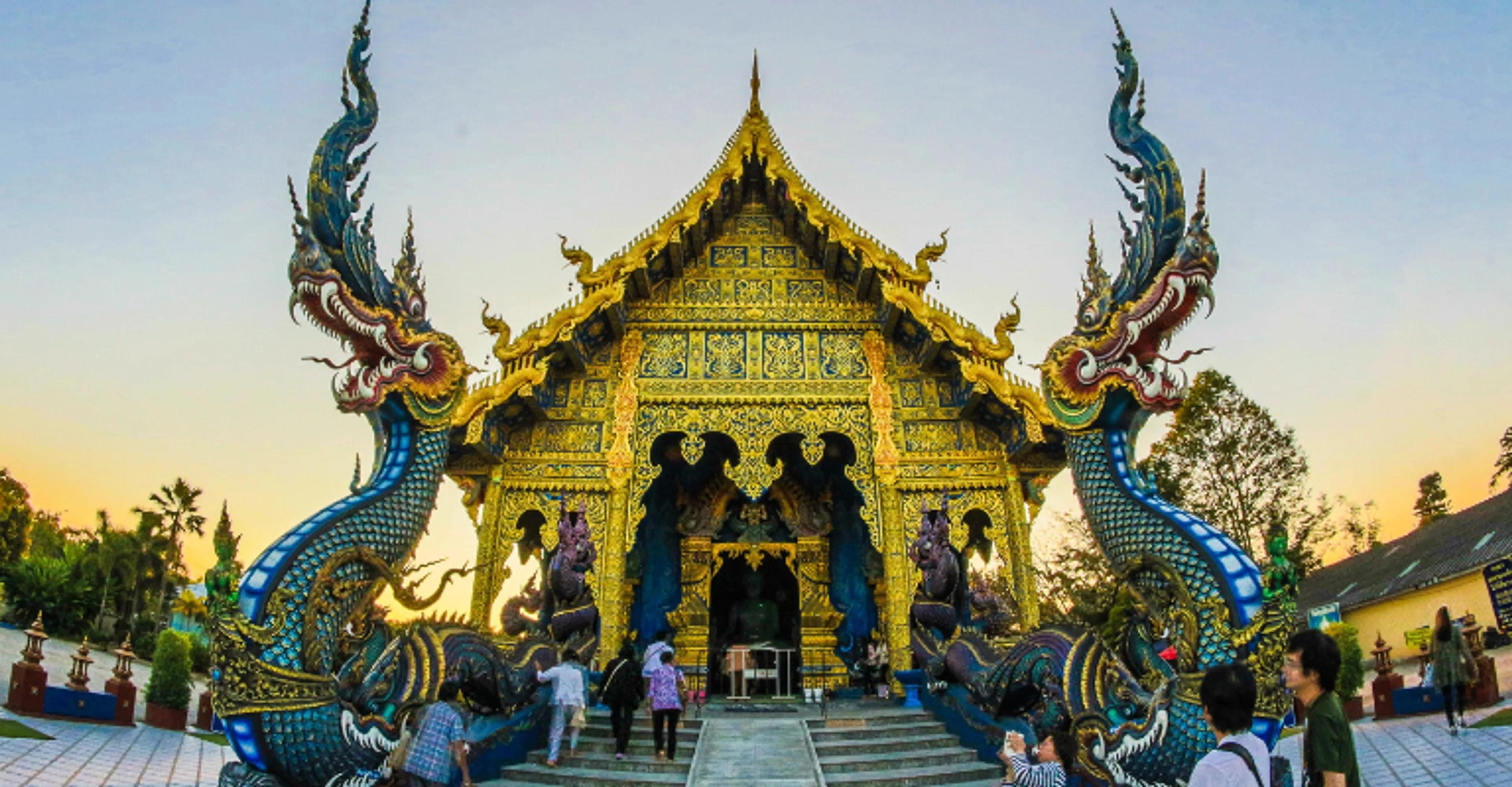 Visitors at the Blue Temple (Wat Rong Suea Ten) with naga serpent statues in Chiang Rai, Thailand