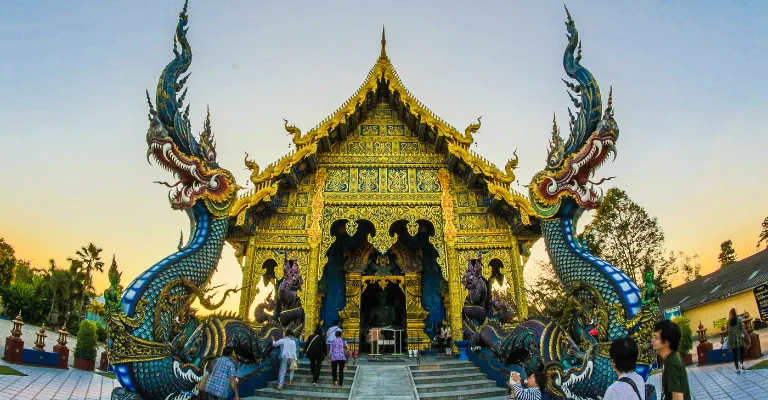 Visitors at the Blue Temple (Wat Rong Suea Ten) with naga serpent statues in Chiang Rai, Thailand