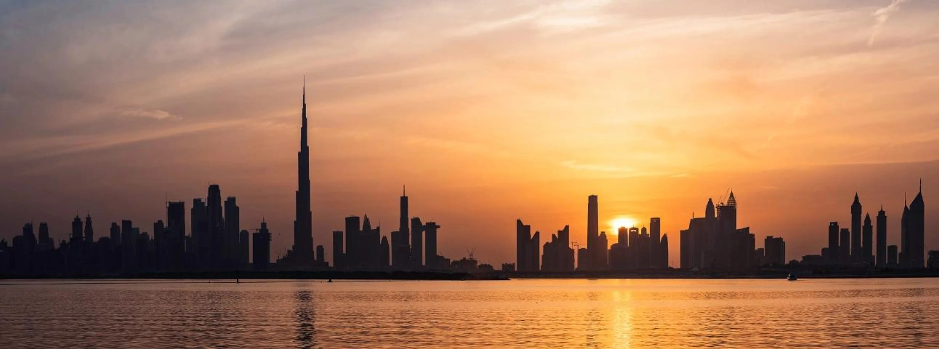 Dubai skyline silhouette with the Burj Khalifa at sunset over the water.