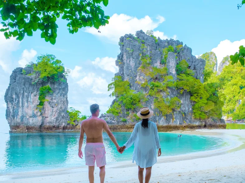 Couple holding hands on a white sand beach facing limestone rocks at Koh Hong, Krabi, Thailand
