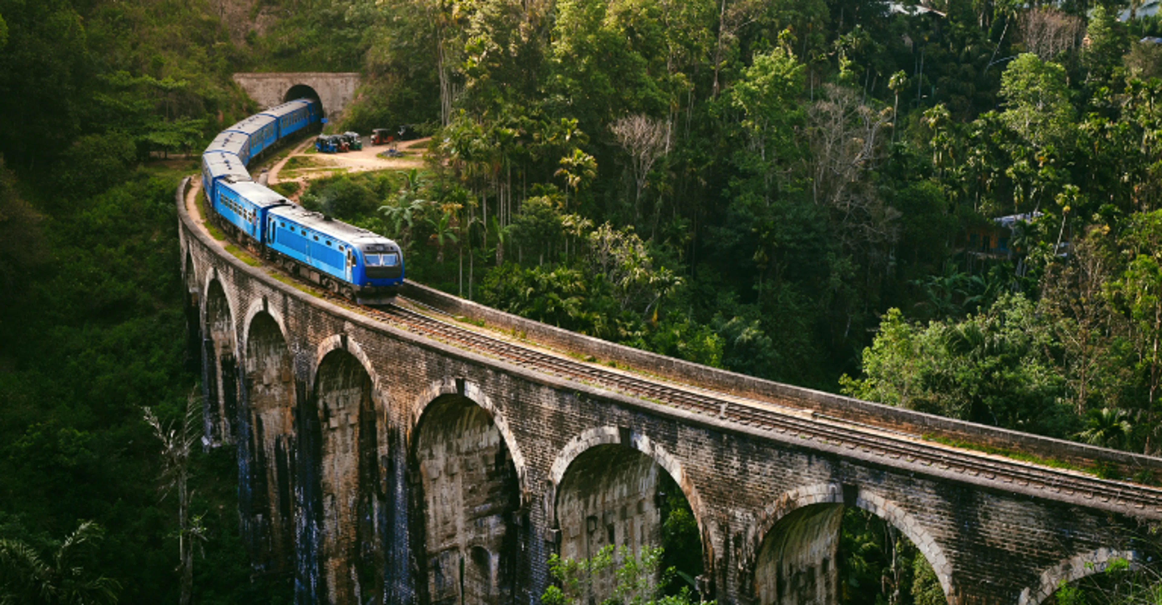 A blue train crossing the Nine Arches Bridge through the hills of Ella