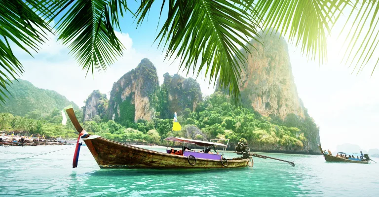 Longtail boats framed by palm leaves near Railay Beach cliffs, Krabi, Thailand