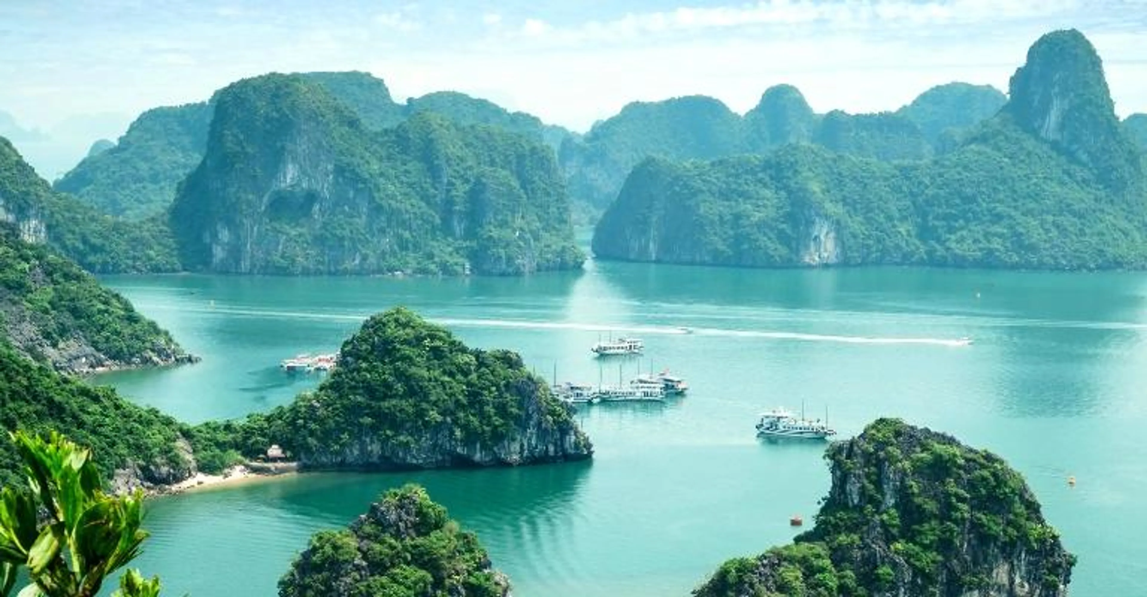 Limestone karst islands rising from turquoise water in Halong Bay, with cruise boats below