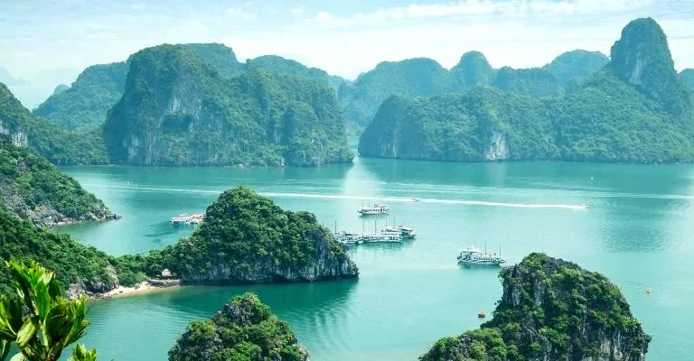 Limestone karst islands rising from turquoise water in Halong Bay, with cruise boats below