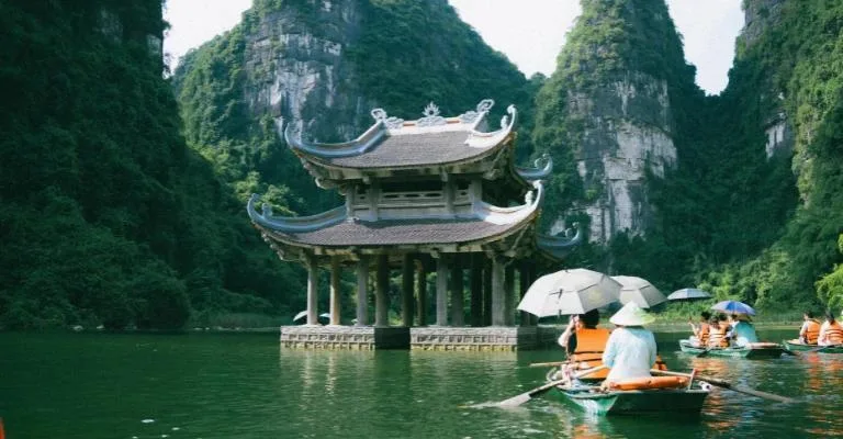 Water pagoda at Trang An surrounded by limestone karsts, tourists boating below