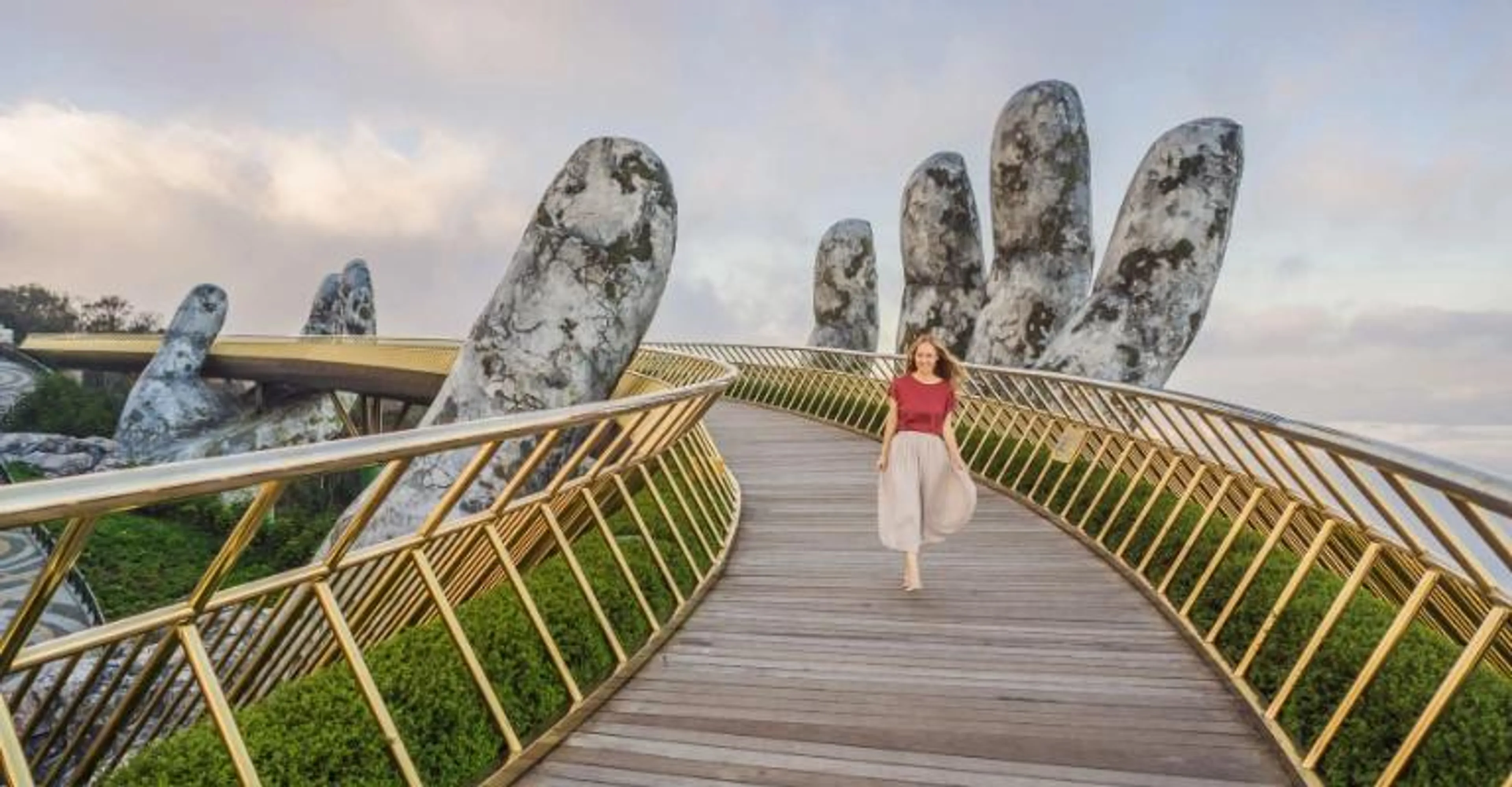 A woman walking across the Golden Bridge, held up by giant stone hands, above Danang