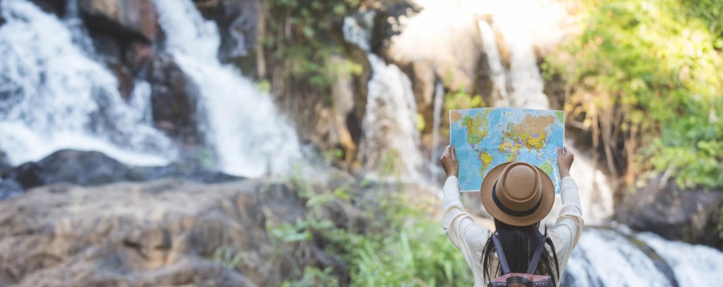 A traveler holding up a map in front of a waterfall.