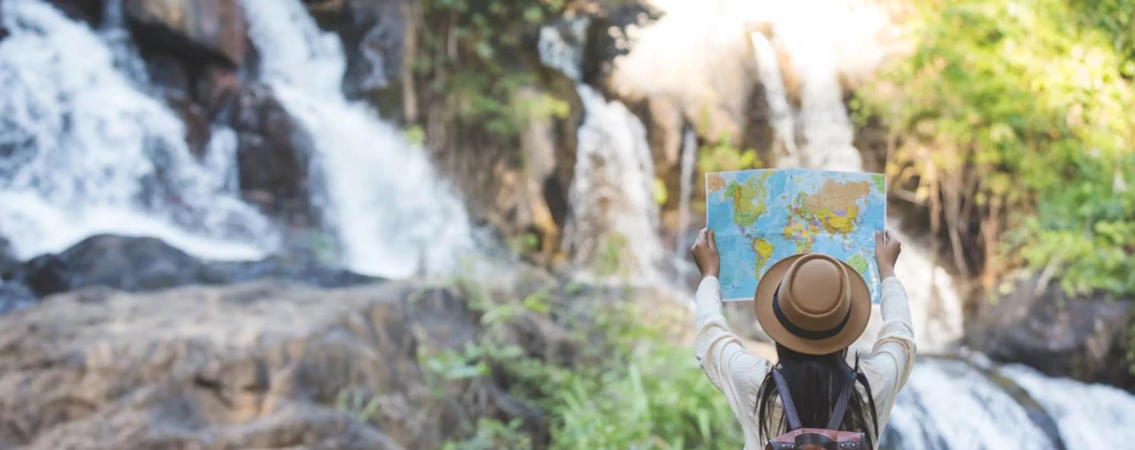 A traveler holding up a map in front of a waterfall.
