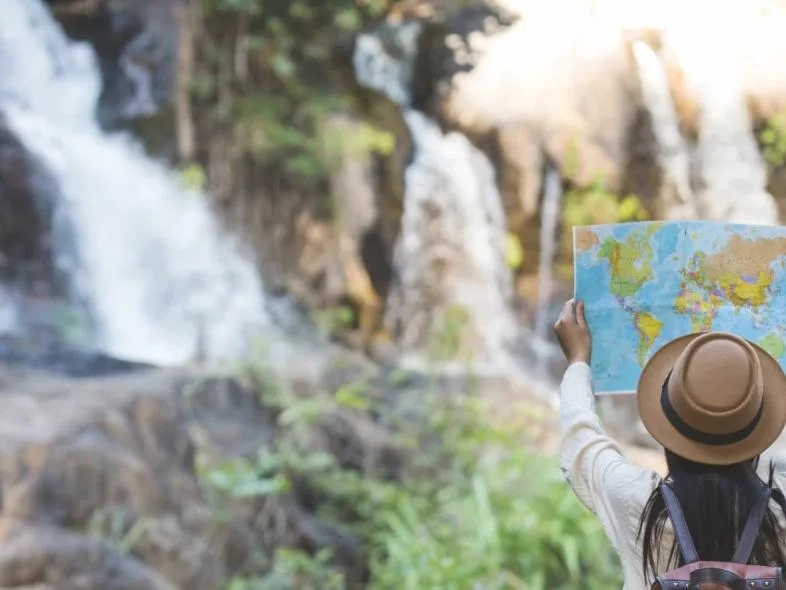 A traveler holding up a map in front of a waterfall.