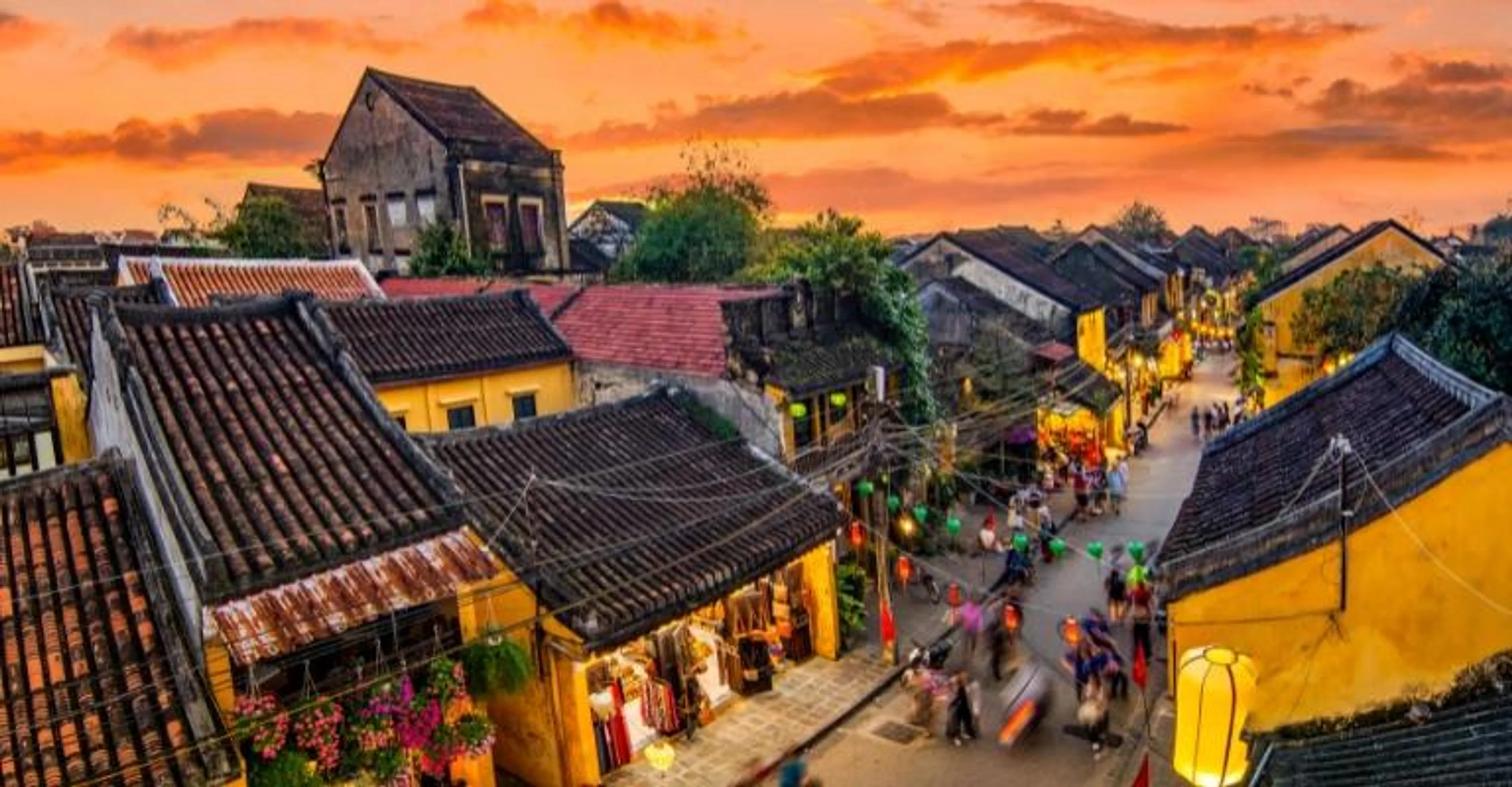 Aerial view over Hanoi's old quarter rooftops and a lantern-strung street at sunset