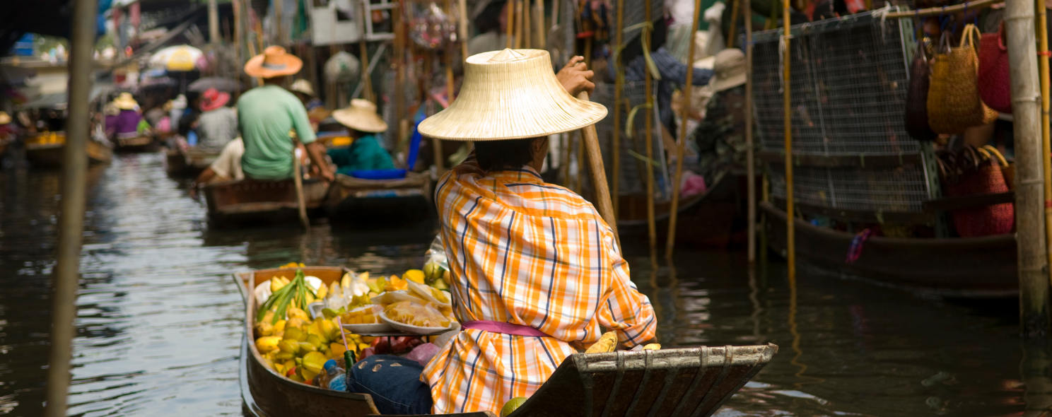 Vendor in a straw hat rowing a fruit-laden boat at a Thai floating market