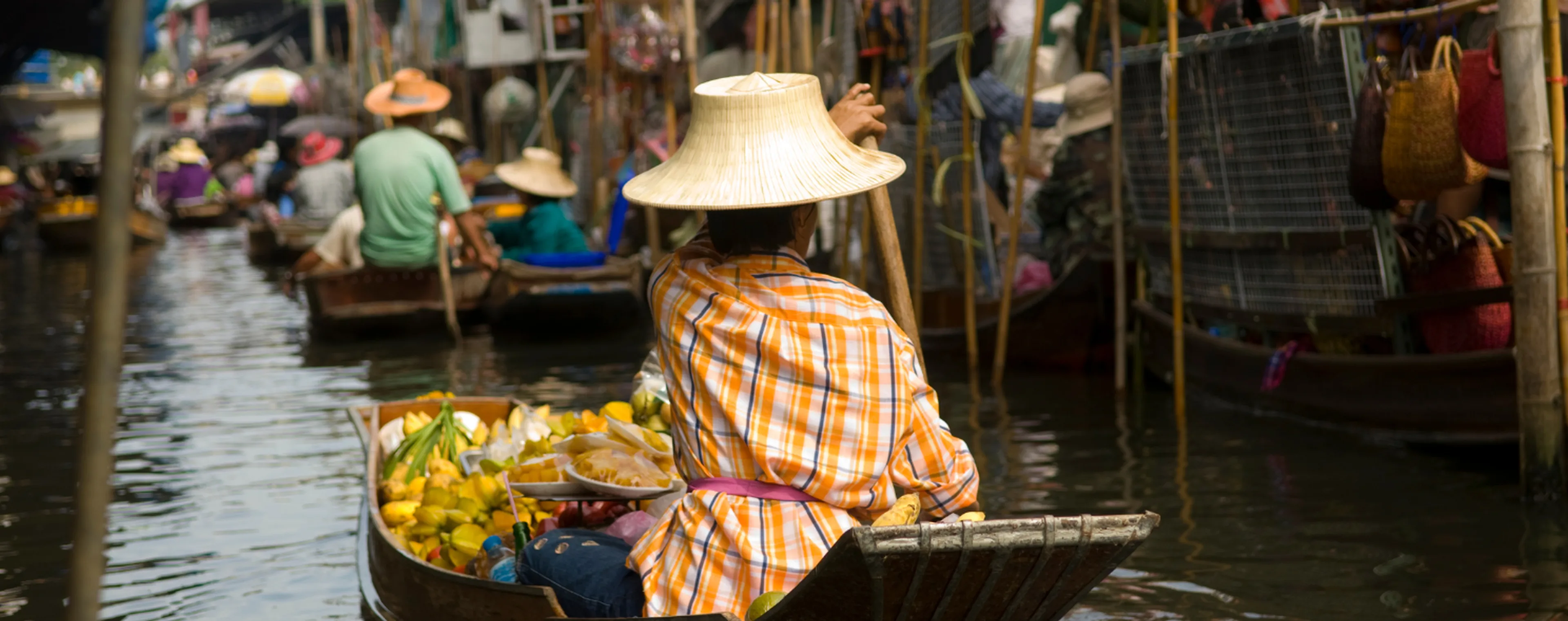 Vendor in a straw hat rowing a fruit-laden boat at a Thai floating market