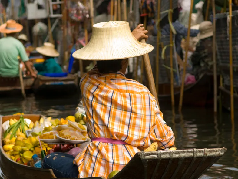 Vendor in a straw hat rowing a fruit-laden boat at a Thai floating market