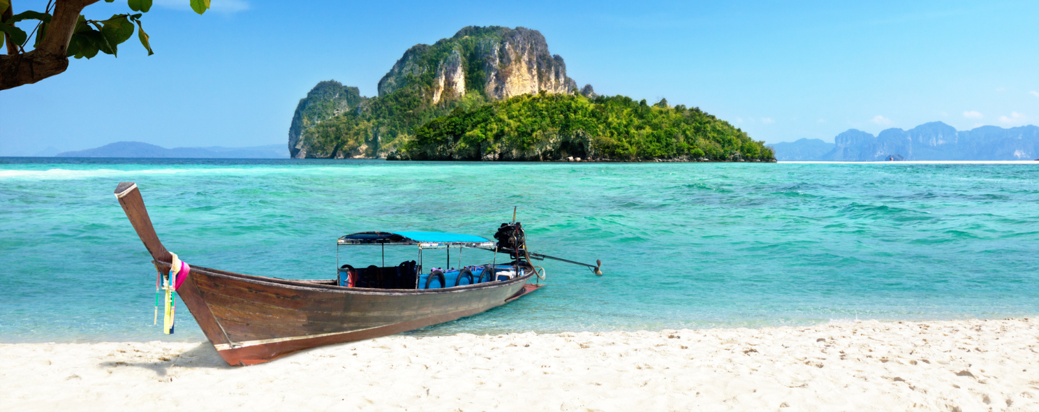 Longtail boat on a white sand beach with a limestone island in Thailand