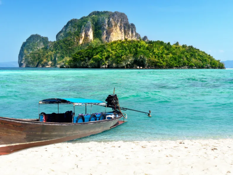 Longtail boat on a white sand beach with a limestone island in Thailand