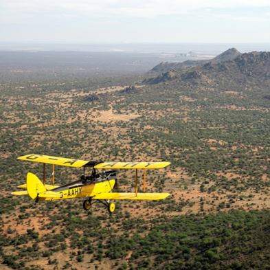 Vintage open-cockpit biplane flying low over rhinos and elephants at Lewa Wildlife Conservancy Kenya