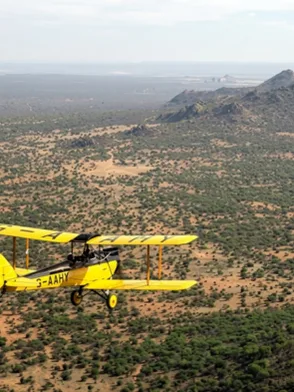 Vintage open-cockpit biplane flying low over rhinos and elephants at Lewa Wildlife Conservancy Kenya