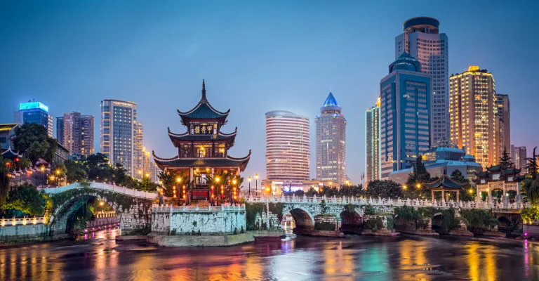 Illuminated skyline of a modern Chinese city with a traditional pagoda and bridge at dusk