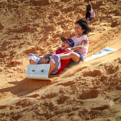 Sandboarder gliding down the golden dunes of Mũi Né at sunset Vietnam
