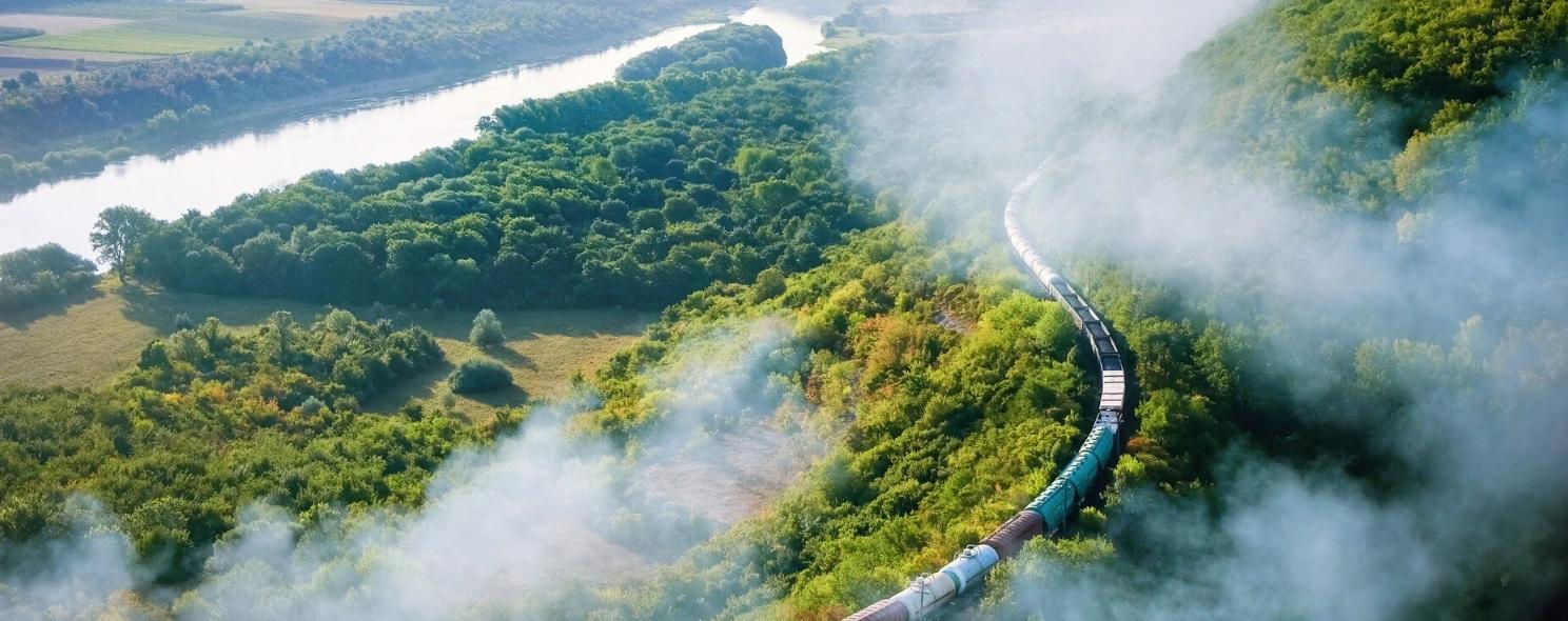 Aerial view of a train winding through misty green hills alongside a river.
