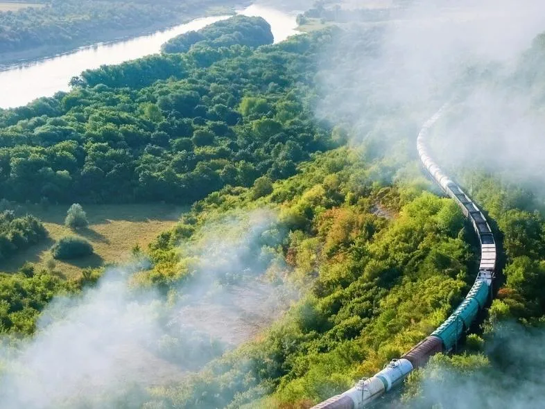 Aerial view of a train winding through misty green hills alongside a river.