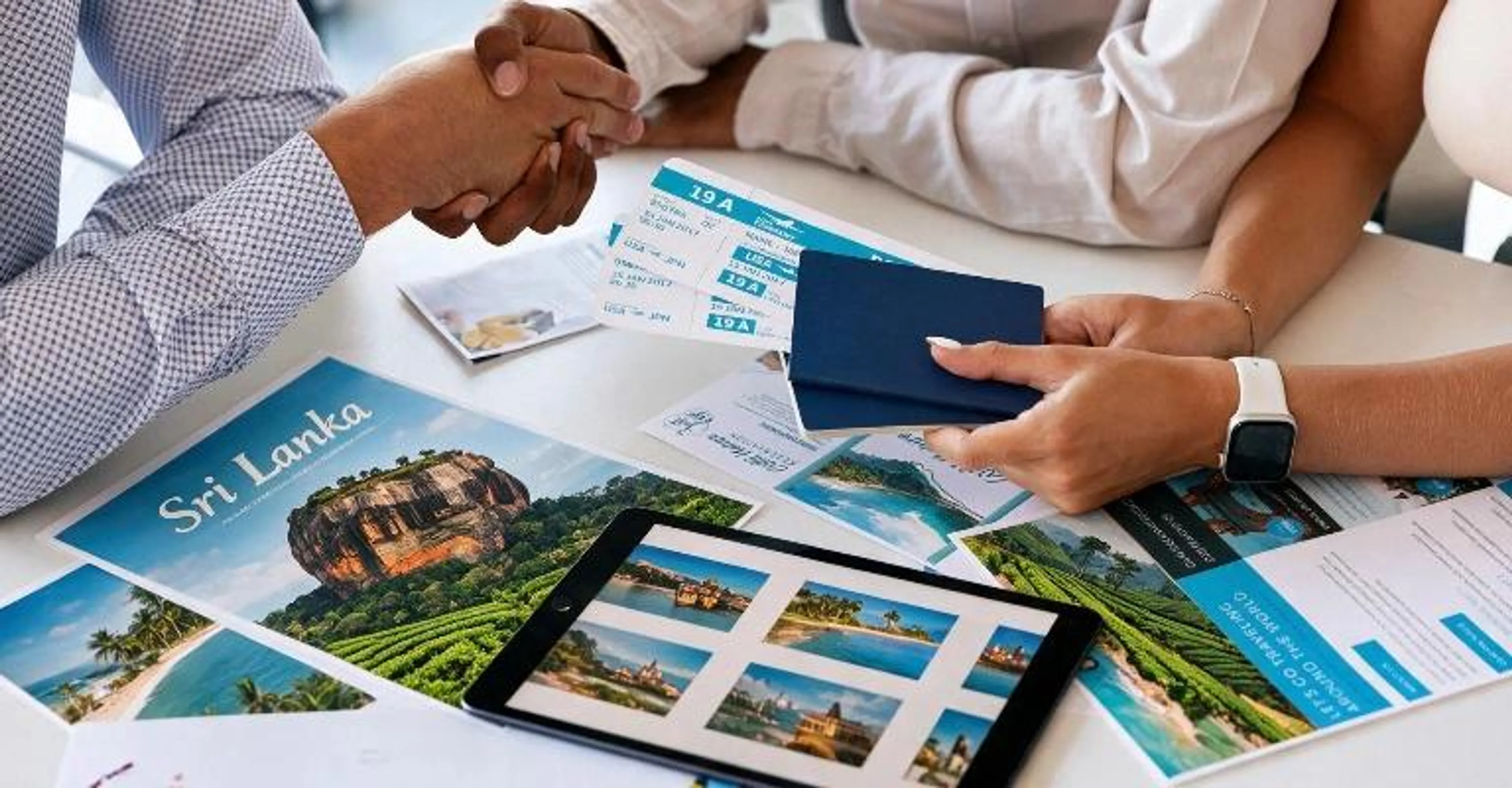 A travel agent shakes hands with a client over a desk with Sri Lanka brochures, tickets, and a passport.