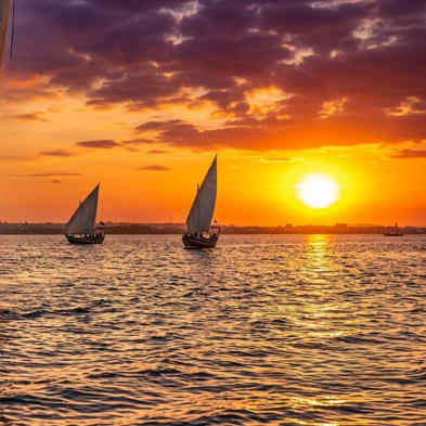 Traditional Swahili wooden dhow sailing past mangroves and stone ruins at sunset in Lamu Kenya