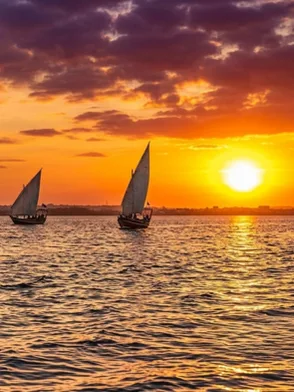 Traditional Swahili wooden dhow sailing past mangroves and stone ruins at sunset in Lamu Kenya