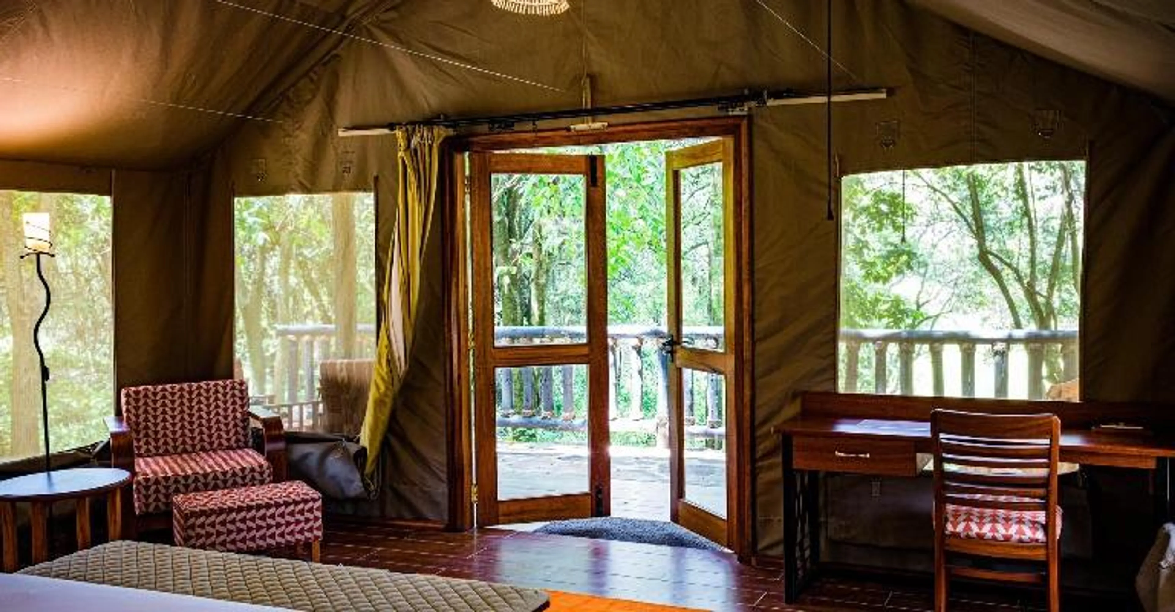 Interior of a luxury safari tent with open doors leading to a forest view.