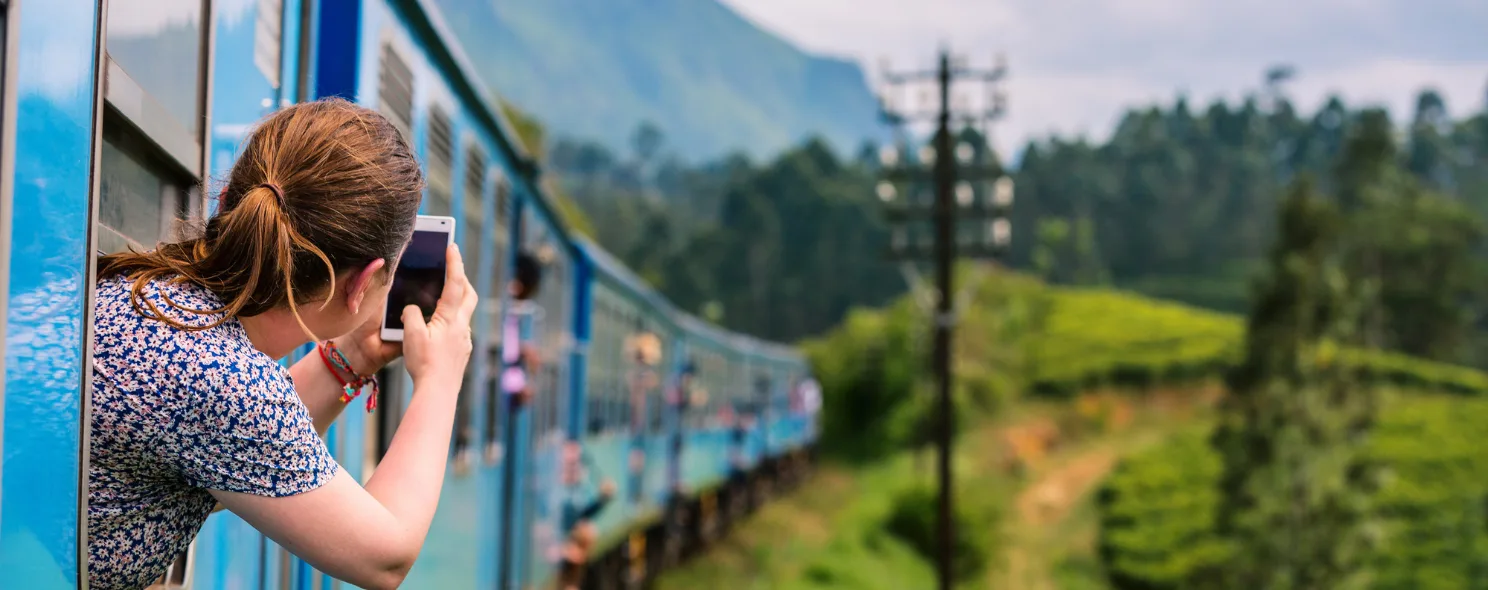 A traveler photographing tea plantations from a train window in Sri Lanka's hill country
