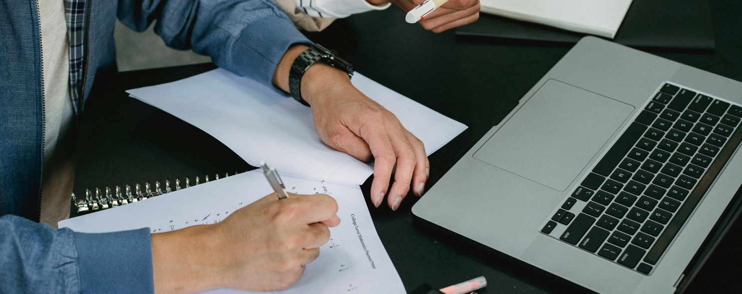Two people reviewing a printed form and taking notes beside an open laptop