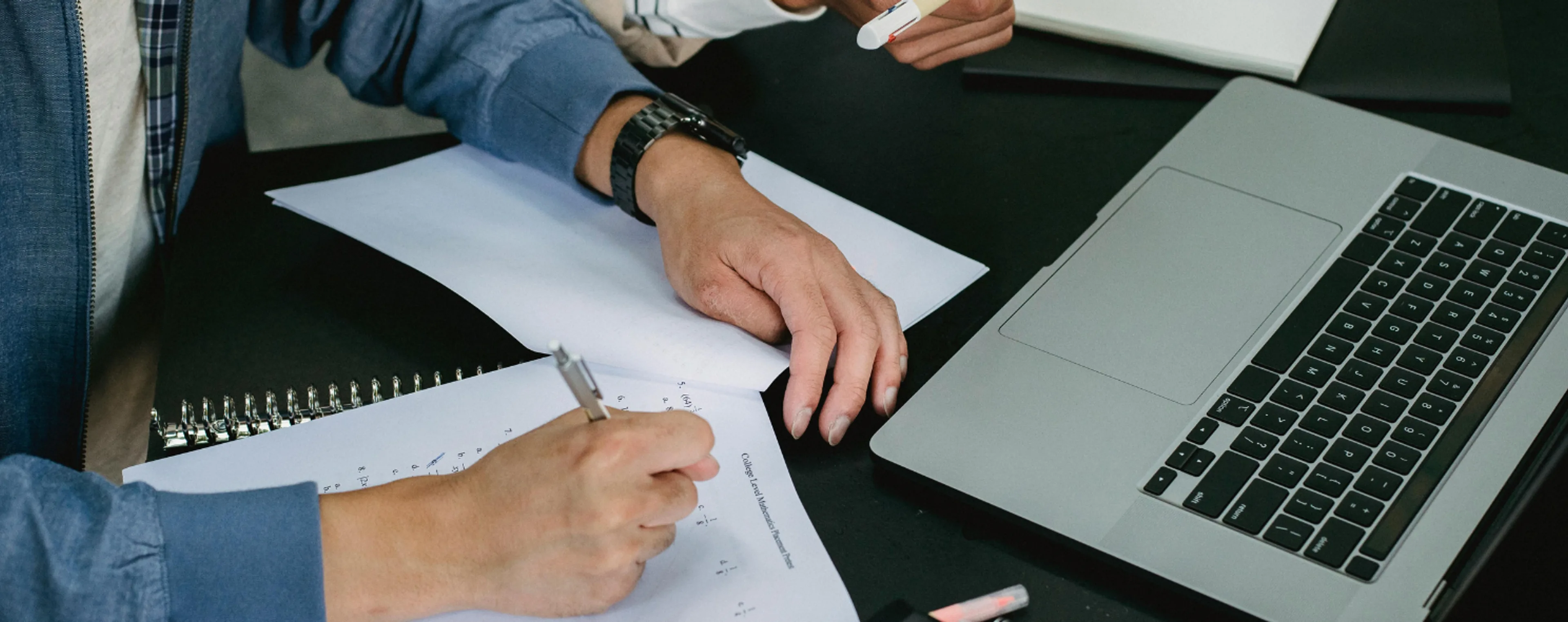 Two people reviewing a printed form and taking notes beside an open laptop