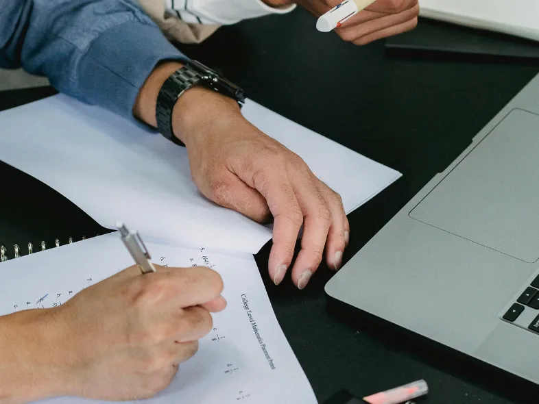 Two people reviewing a printed form and taking notes beside an open laptop