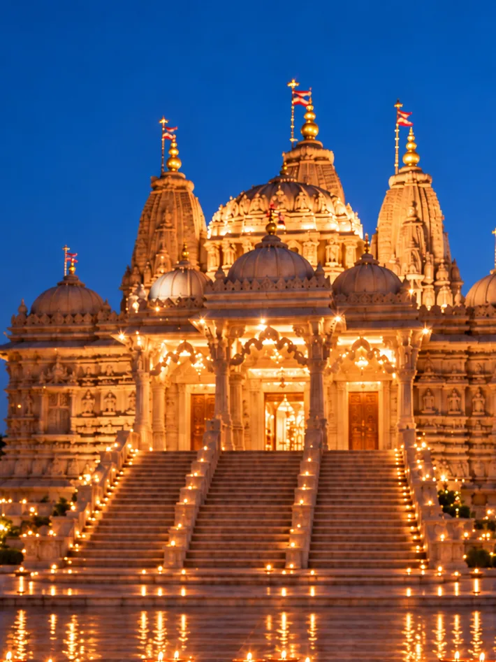 Indian family lighting diyas around a colorful rangoli in front of an illuminated Hindu temple during Diwali.