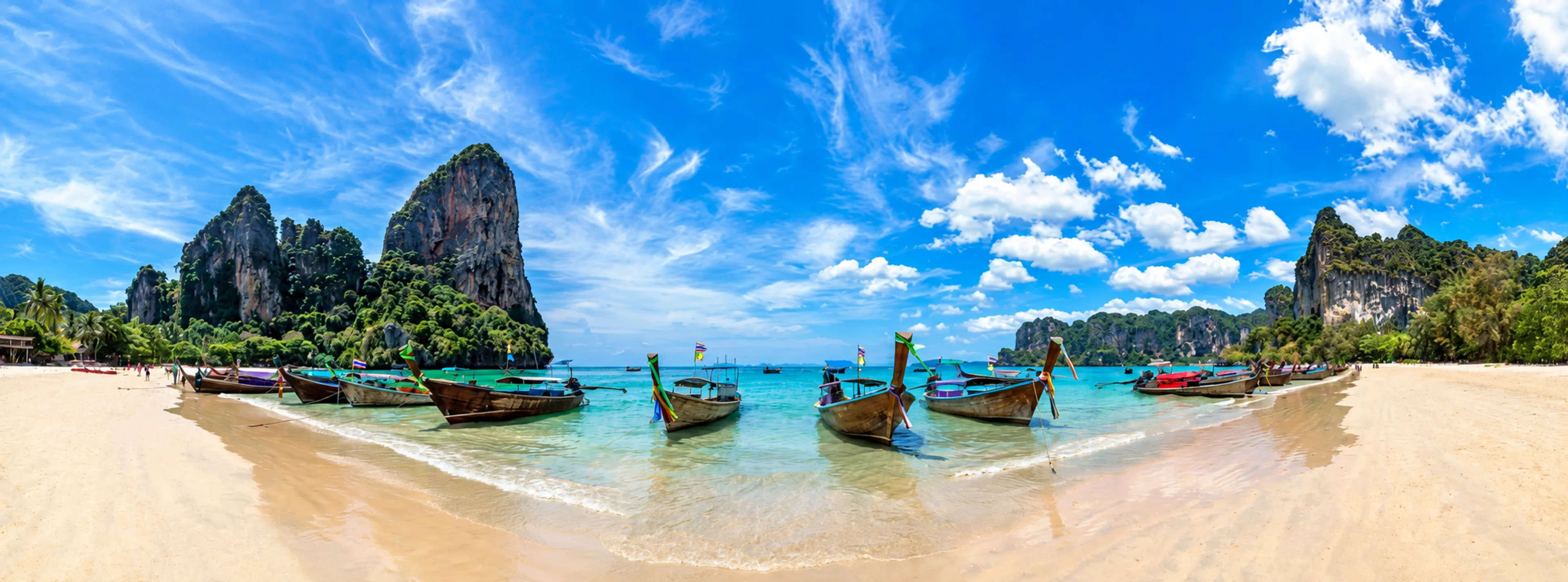 Longtail boats anchored at a white sand beach between limestone cliffs.